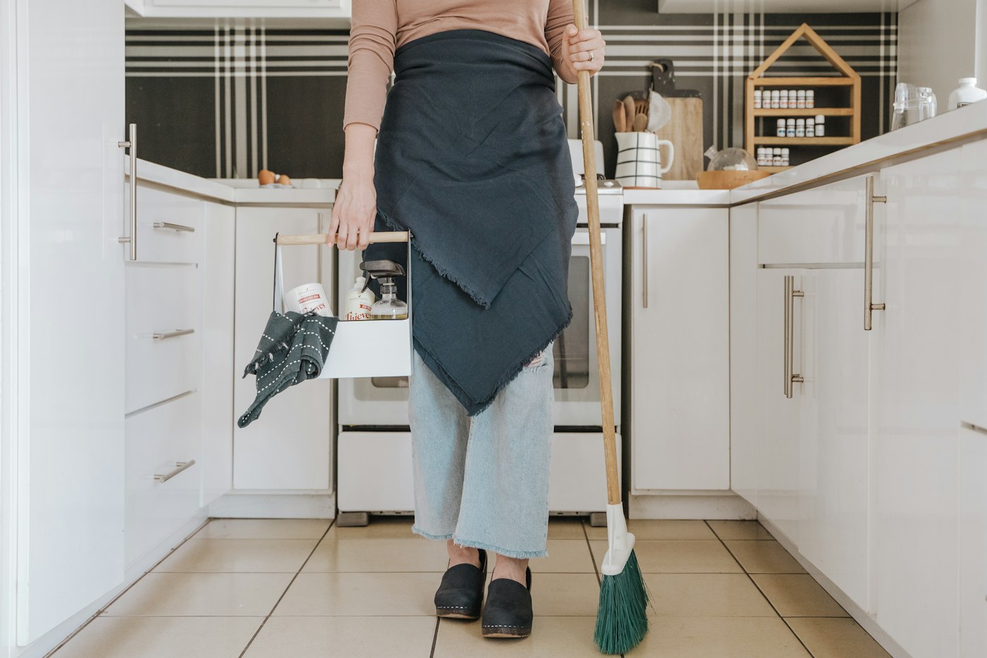 Cleaner with a supply caddy and broom in a white kitchen